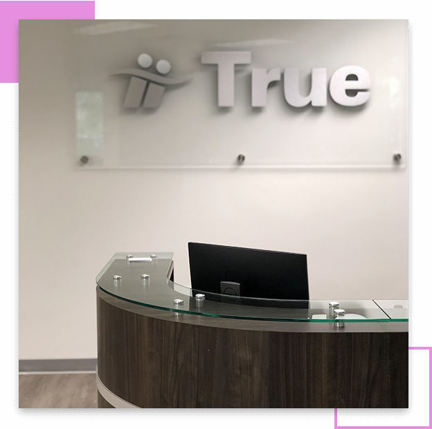 Curved glass reception desk beneath "True" sign